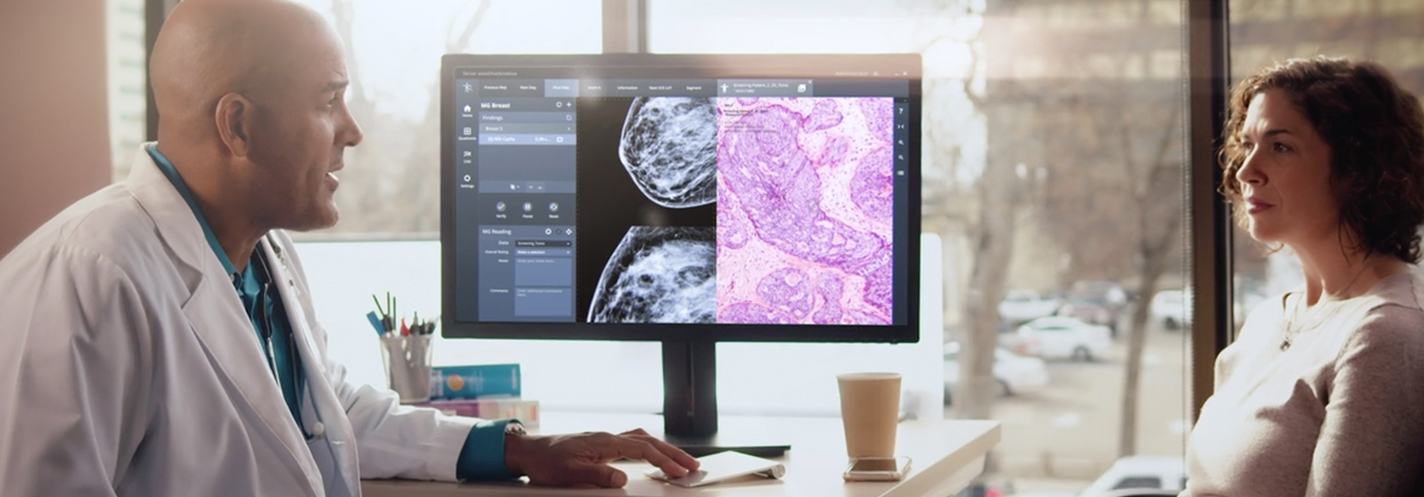 An oncologist speaking with a patient reviewing a diagnosis on a monitor