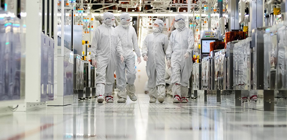 Fabrication plant workers in clean suits walking down a hallway